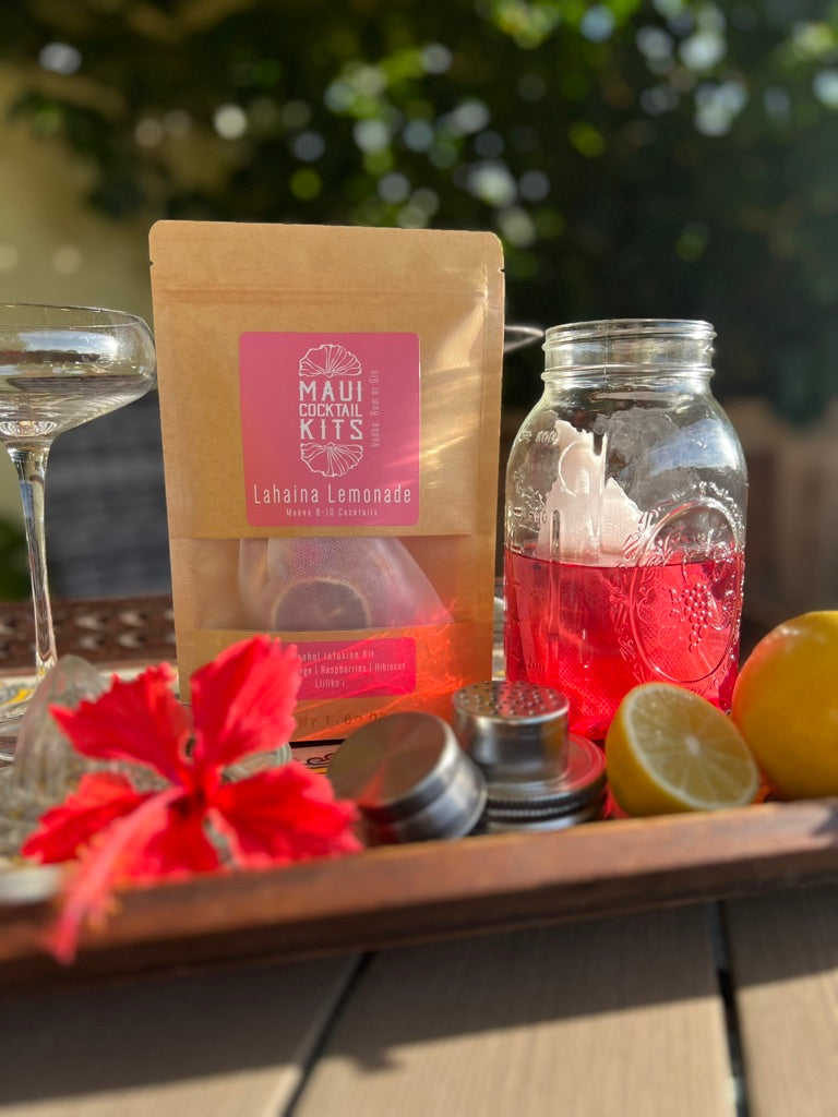Maui Cocktail lemonade kit with a tropical cocktail, lemons, and a flower on a wooden surface.